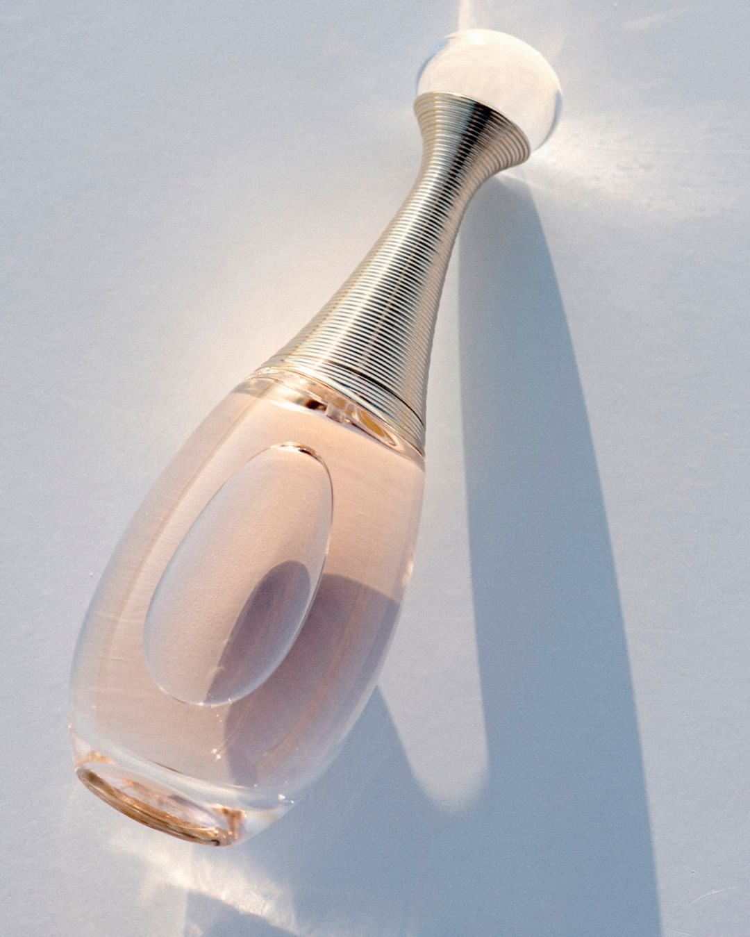 Perfume bottle of J'adore Dior on a white surface with visible shadow and highlights.