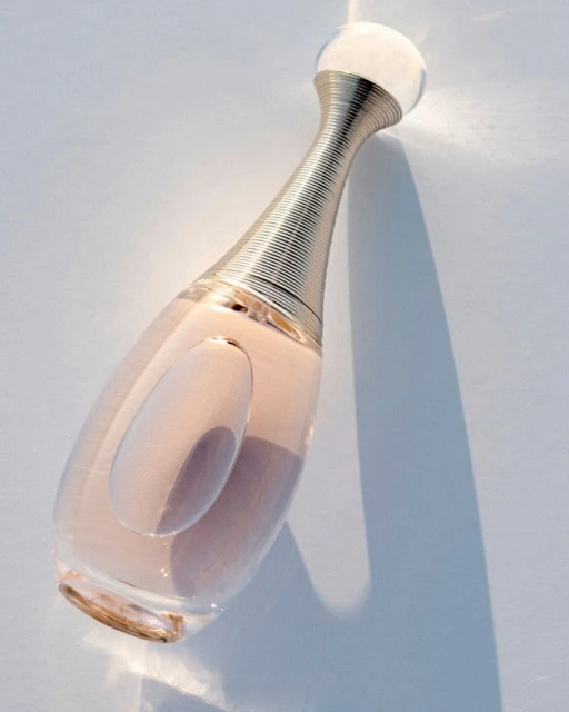 Perfume bottle of J'adore Dior on a white surface with visible shadow and highlights.