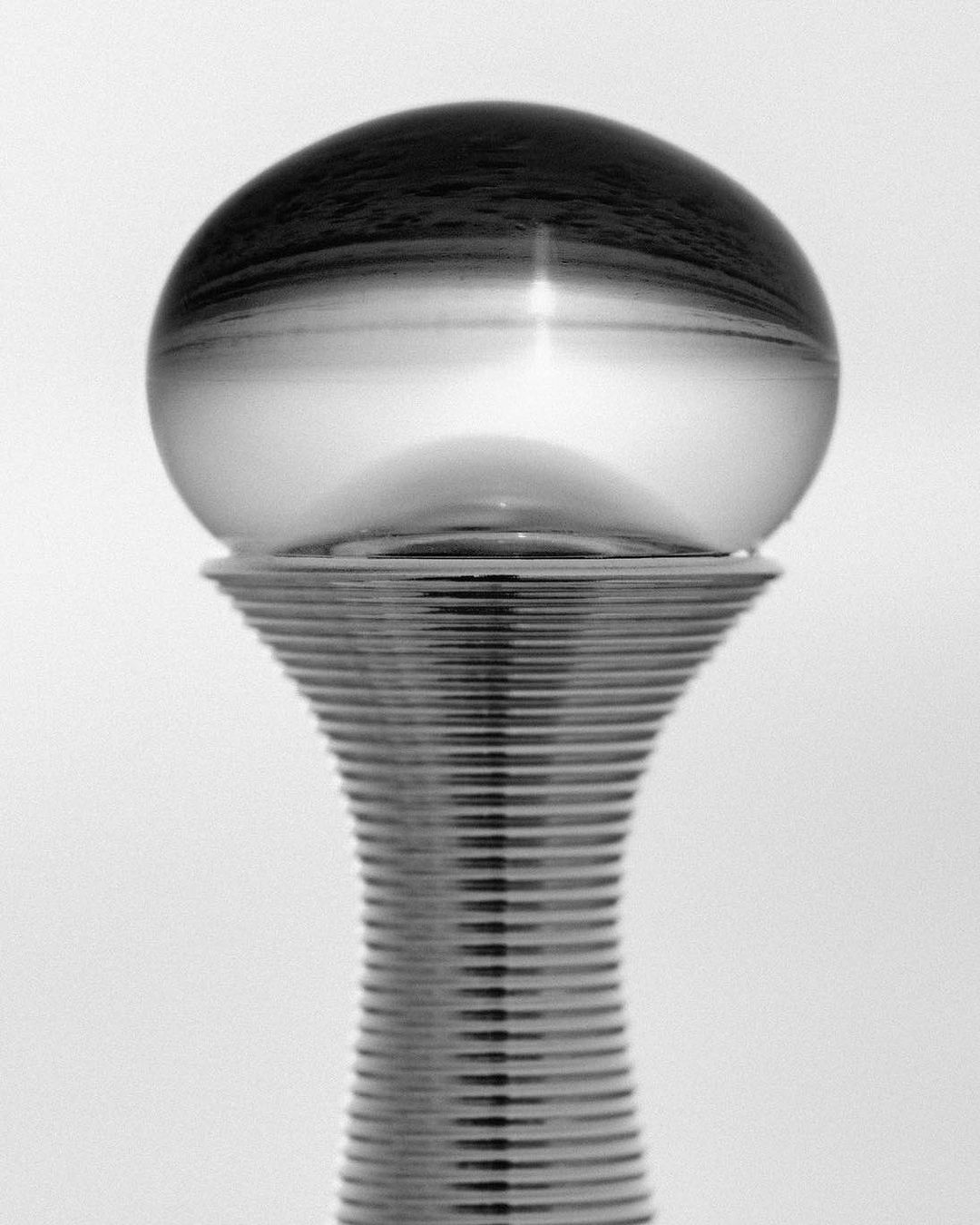 Monochrome photograph of a crystal ball sitting atop a silver pedestal with a rippled design, set against a plain white background.