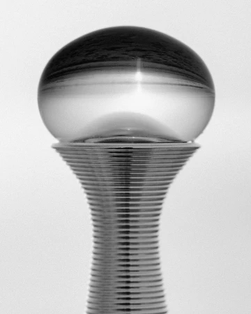 Monochrome photograph of a crystal ball sitting atop a silver pedestal with a rippled design, set against a plain white background.