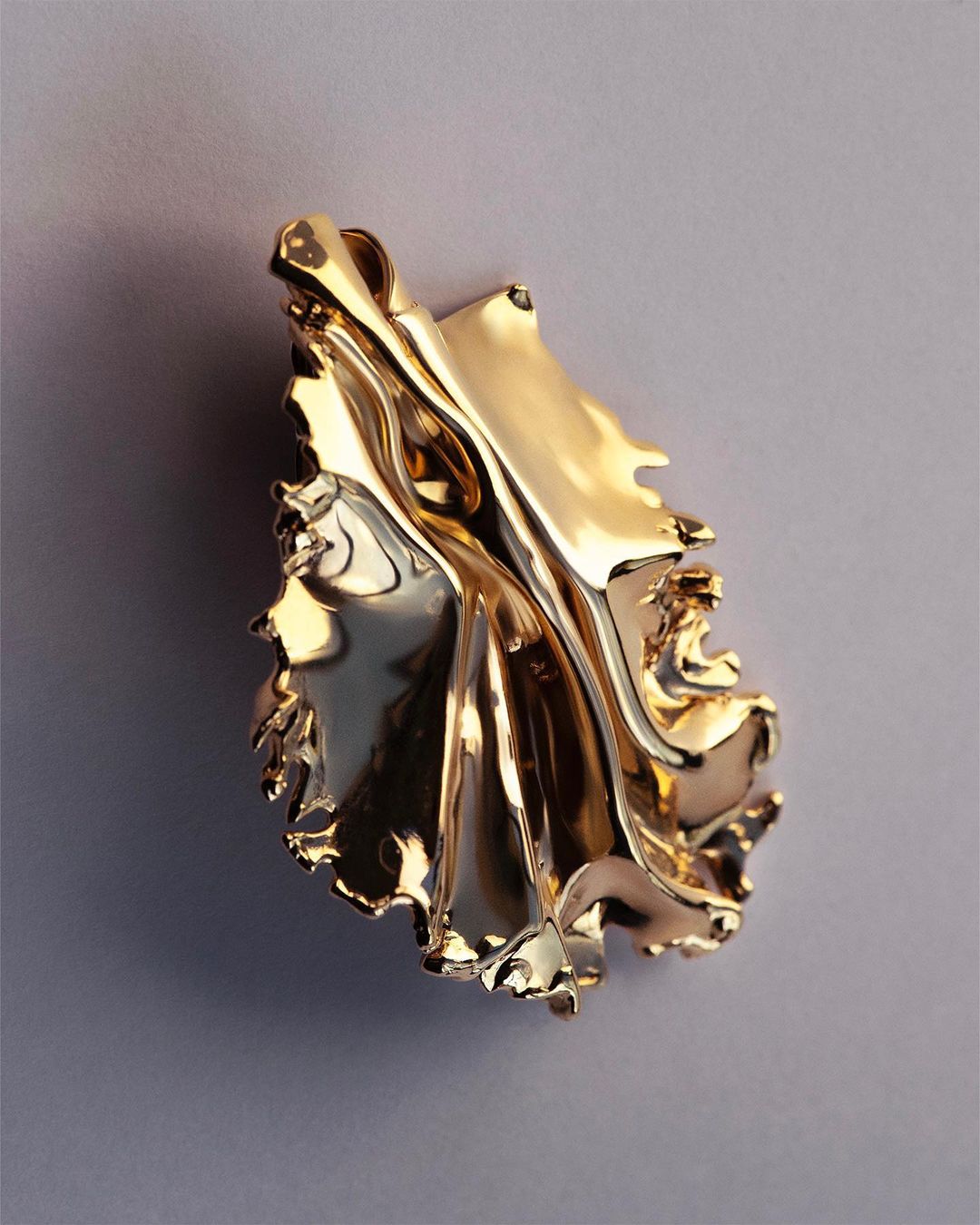 Elegant golden leaf sculpture with shiny surface, gracefully suspended against a muted gray background in a vertically oriented shot.