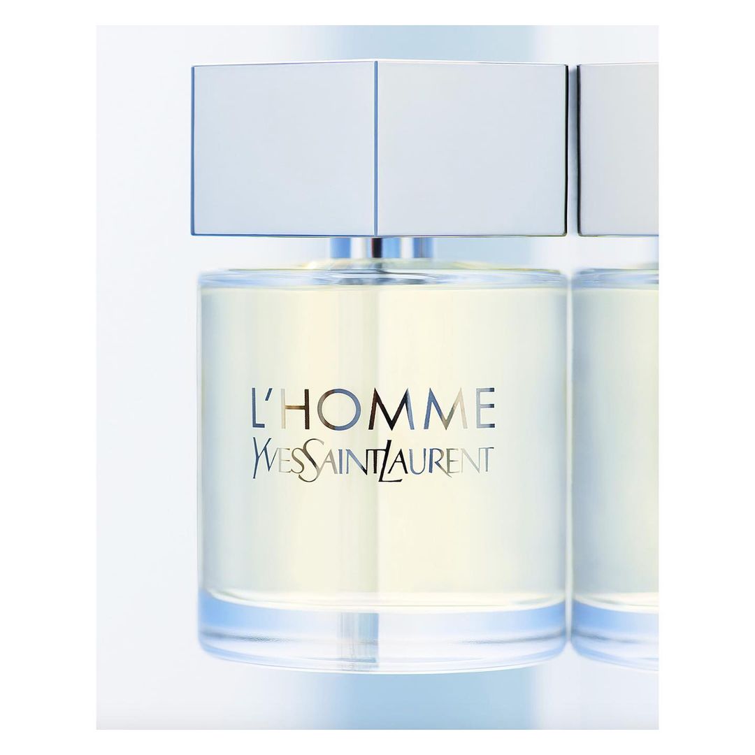 Close-up studio shot of a clear glass bottle of L'Homme Yves Saint Laurent fragrance with a silver cap on a white background.