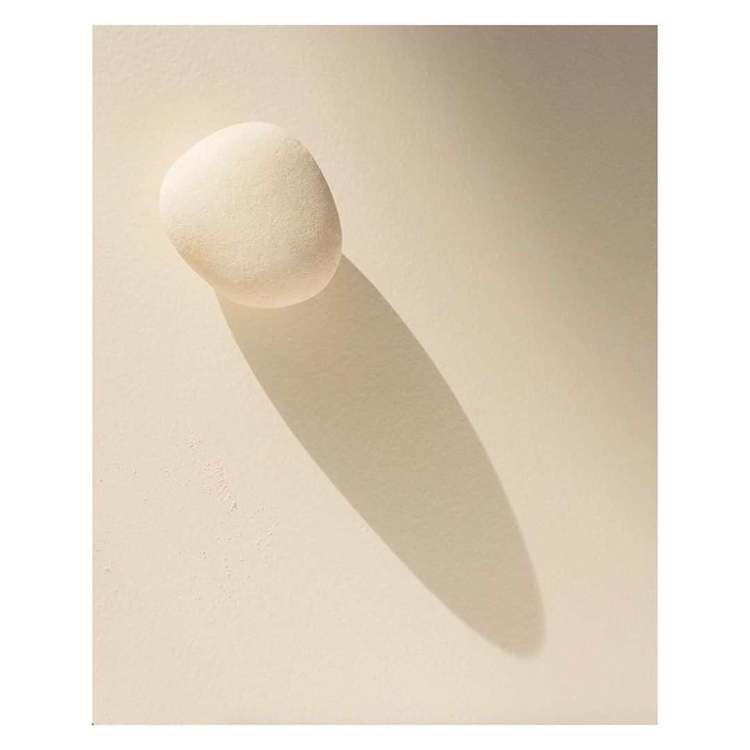 Smooth white stone on a pale surface with a distinct shadow, showcasing minimalist design and a clean aesthetic in natural light.