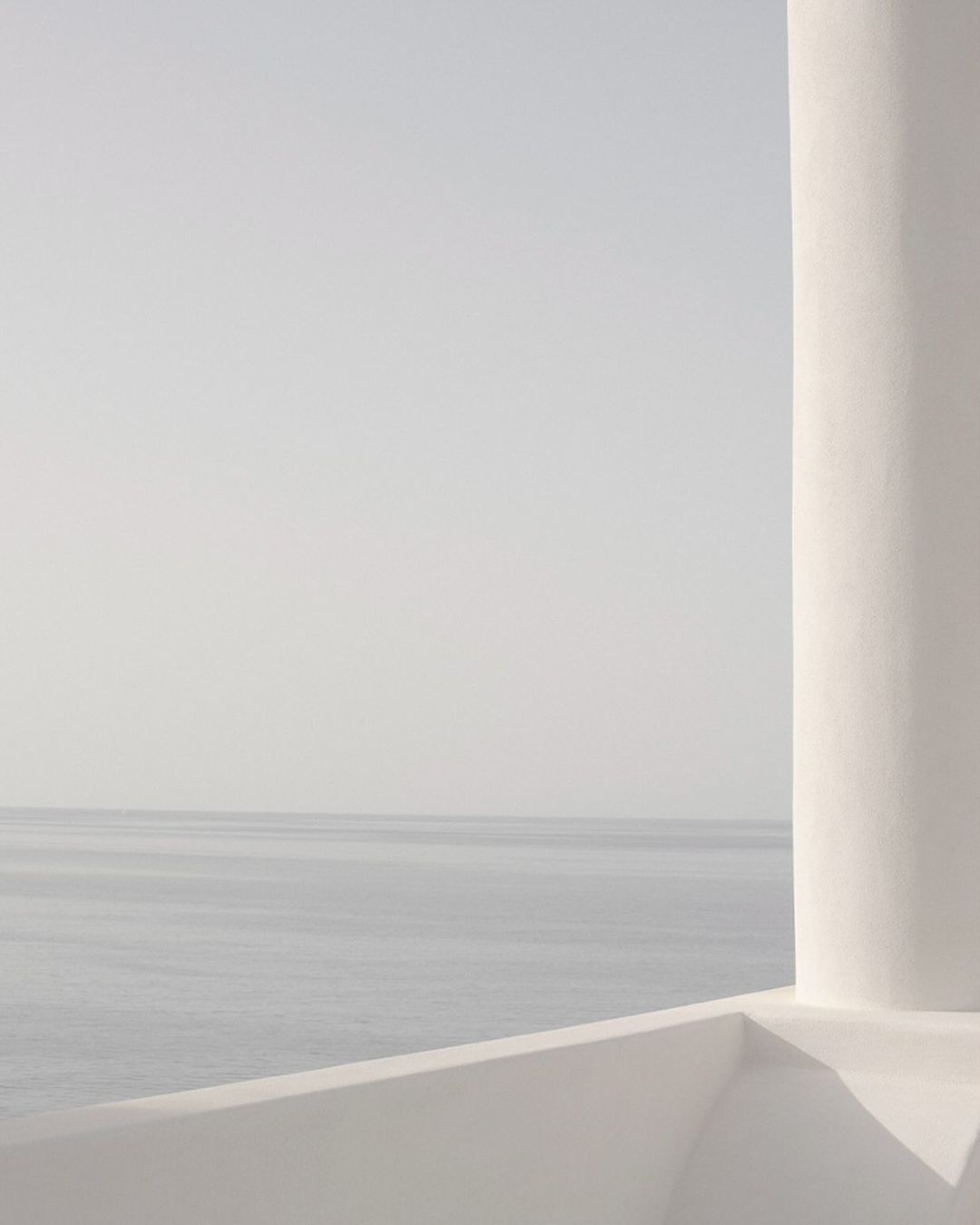 Minimalist view of the sea and sky from a white terrace with a rounded architectural column, creating a serene and clean aesthetic.