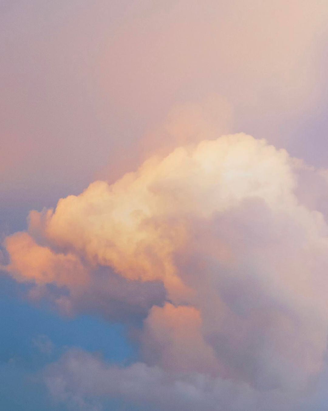 Dramatic cloudscape with puffy cumulus clouds in soft pastel hues of pink, peach, blue, and purple creating a dreamy, ethereal scene.