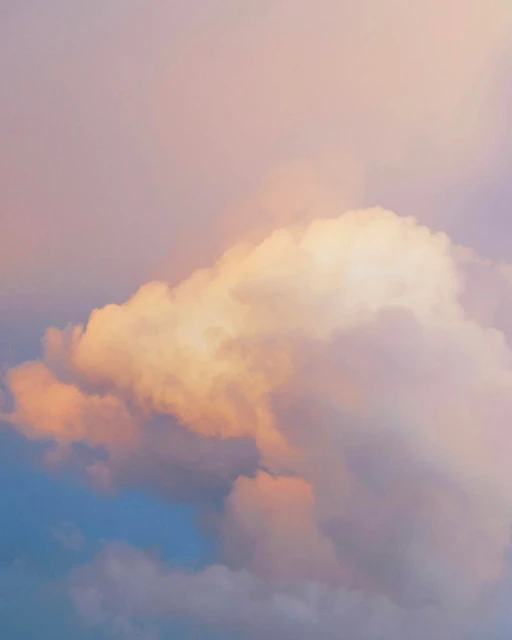 Dramatic cloudscape with puffy cumulus clouds in soft pastel hues of pink, peach, blue, and purple creating a dreamy, ethereal scene.