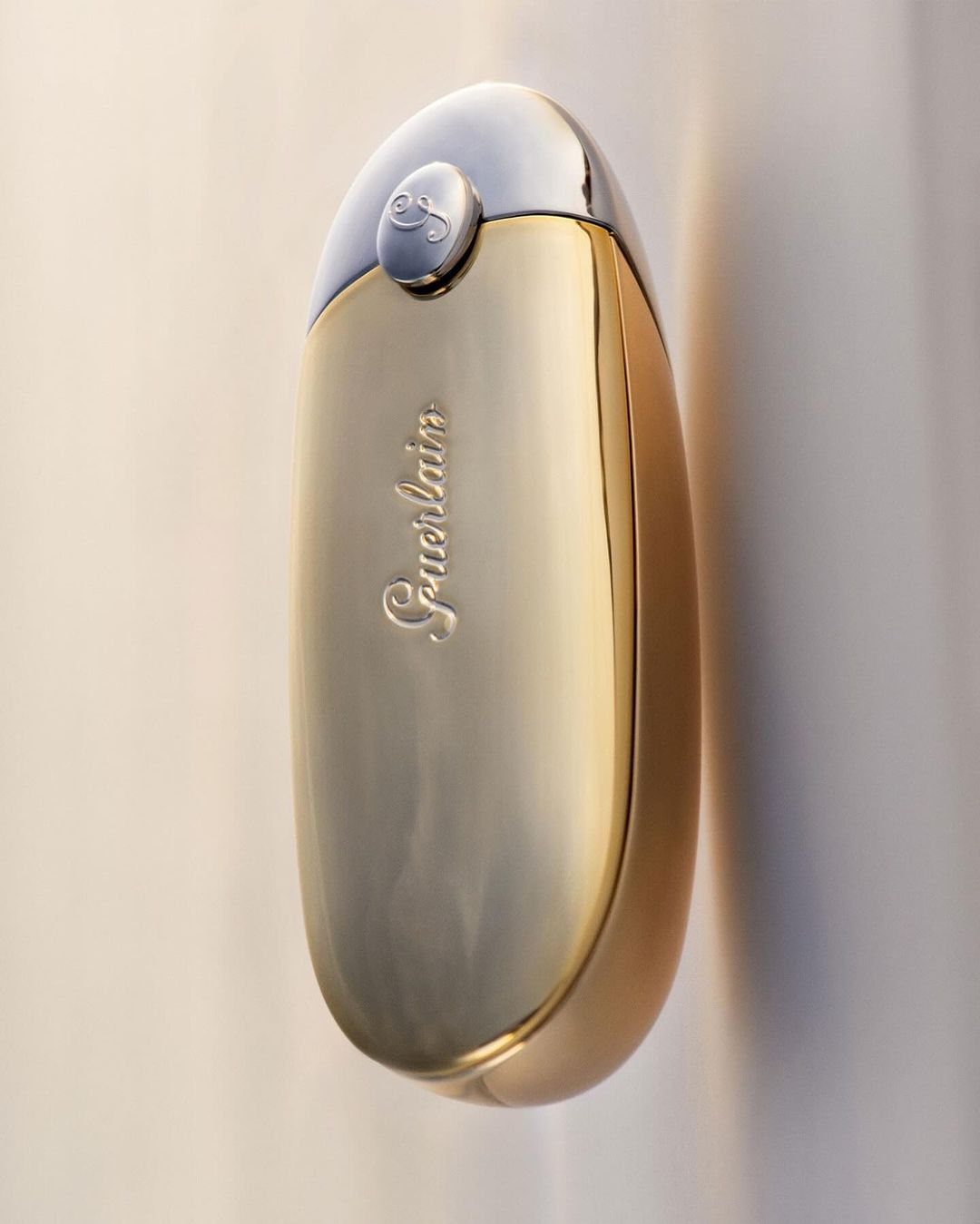 Elegant studio shot of a gold and silver perfume bottle by Guerlain, highlighting its curved shape and reflective surface against a light backdrop.
