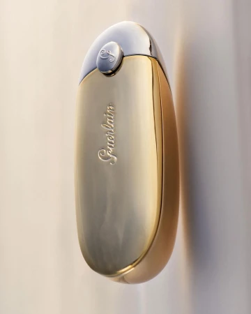 Elegant studio shot of a gold and silver perfume bottle by Guerlain, highlighting its curved shape and reflective surface against a light backdrop.