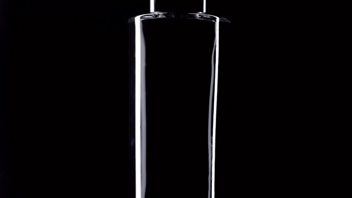 Close-up studio shot of a transparent glass cylinder against a stark black background, highlighting its smooth surface and geometric shape.