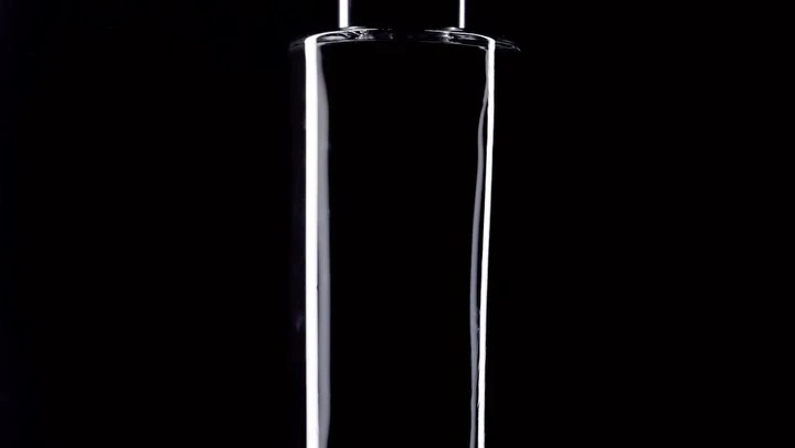 Close-up studio shot of a transparent glass cylinder against a stark black background, highlighting its smooth surface and geometric shape.