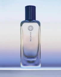 Vertical product shot of a rectangular perfume bottle with purple cap set against a soft gradient background in Paris