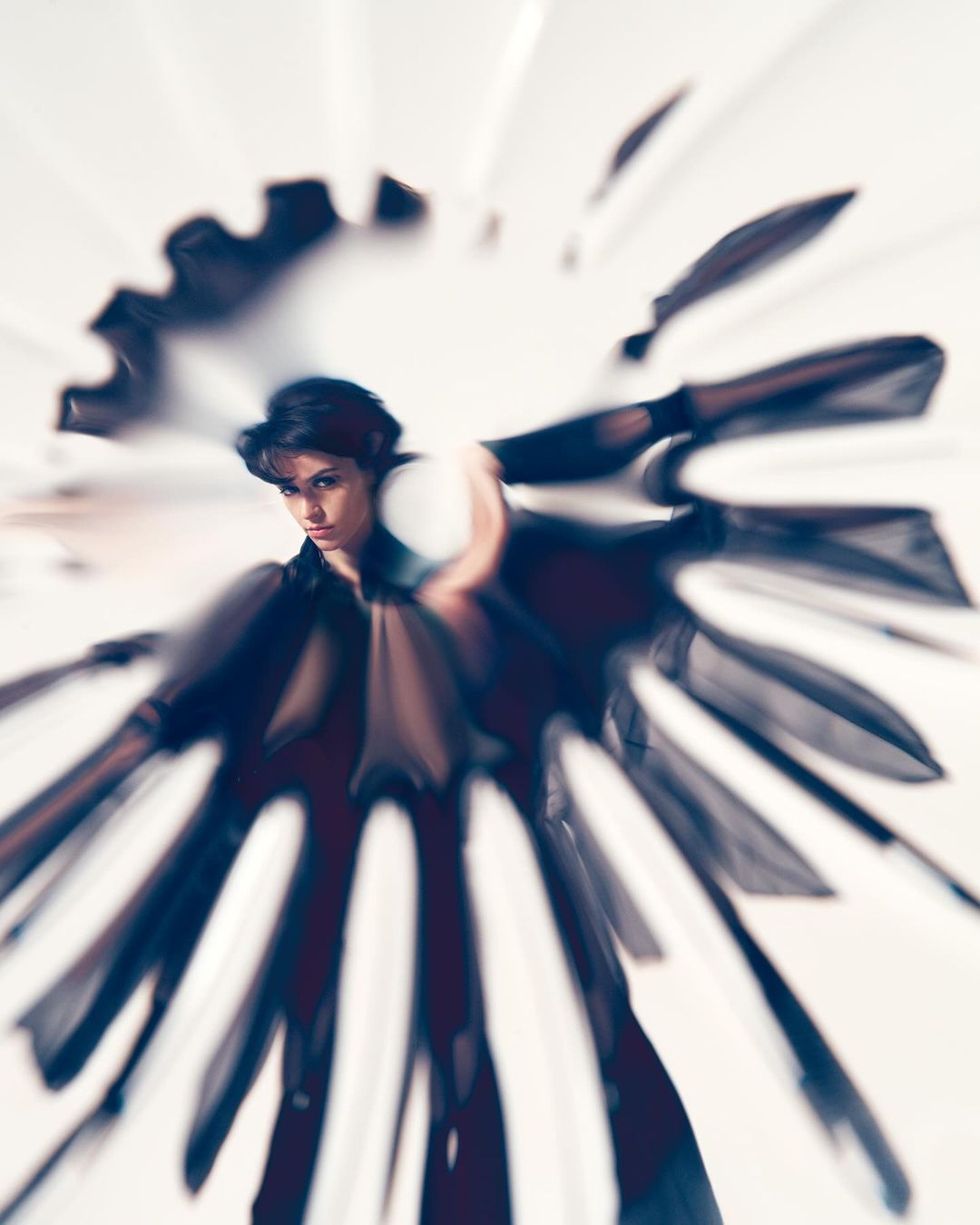 Woman in black sheer fabric posing with blurred zoom effect in a brightly lit indoor studio.
