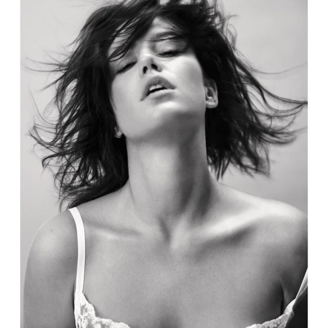 Black and white portrait of an adult woman with flowing hair. She is in lingerie with her eyes closed in an indoor setting.