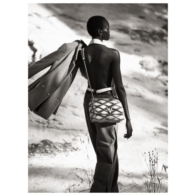 Black and white fashion shot of a slender, dark-skinned woman with short hair walking in nature wearing a designer handbag.