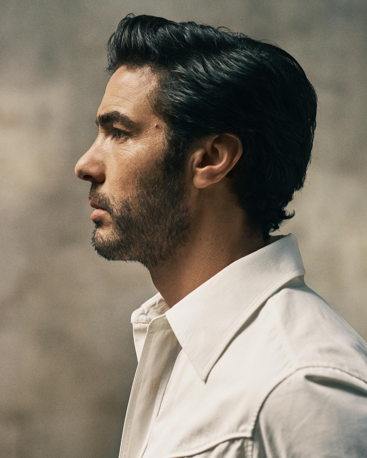 Portrait of an adult male in a white shirt against a neutral backdrop, captured in a medium shot with shallow depth of field.