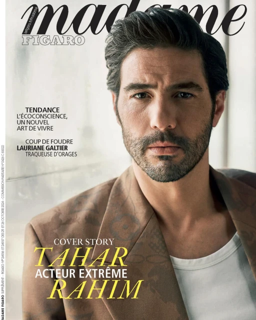 Magazine cover featuring a man with dark hair and a beard, wearing a blazer and white undershirt, posing against a blurred backdrop.