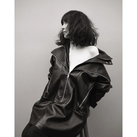 Monochrome portrait of a woman with dark hair wearing an oversized leather jacket against a plain background.