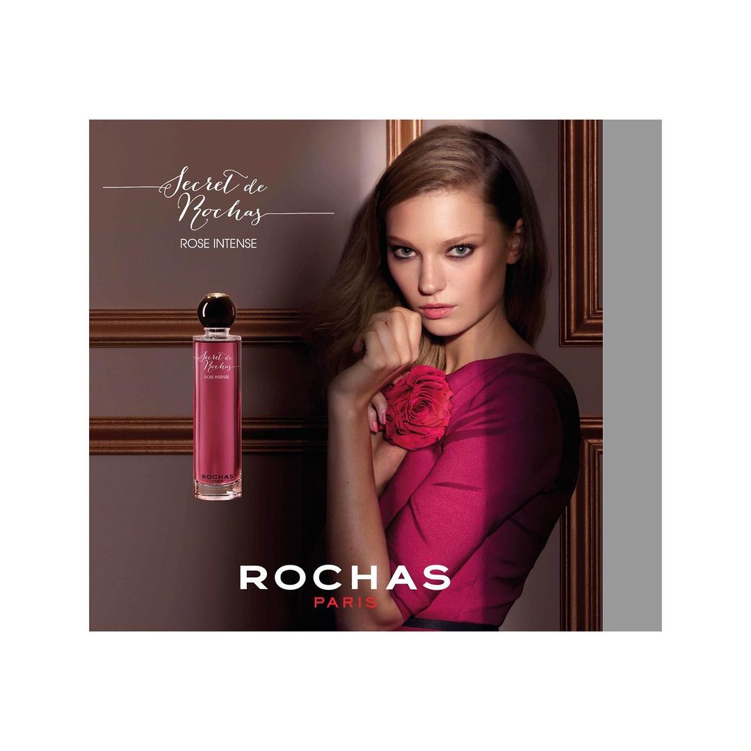 Woman in pink dress holding a red rose next to a perfume bottle in a beauty advertising campaign by Thiemo Sander