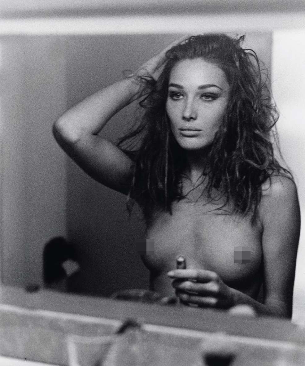Black-and-white portrait of a woman fixing her hair while holding lipstick, reflected in a mirror, capturing a timeless beauty scene.