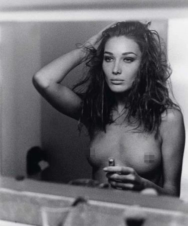 Black-and-white portrait of a woman fixing her hair while holding lipstick, reflected in a mirror, capturing a timeless beauty scene.
