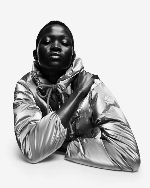 Black and white portrait of a person wearing a shiny puffer jacket with their arm across their body in a photo studio setting.