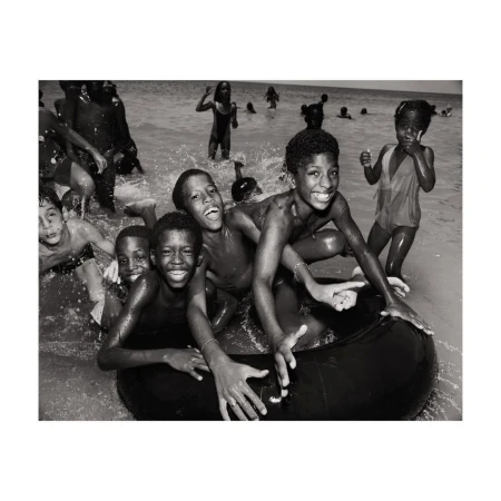A group of Black children in water, some with an inner tube, smiling with a monochrome aesthetic creating a vintage, joyful beach scene.