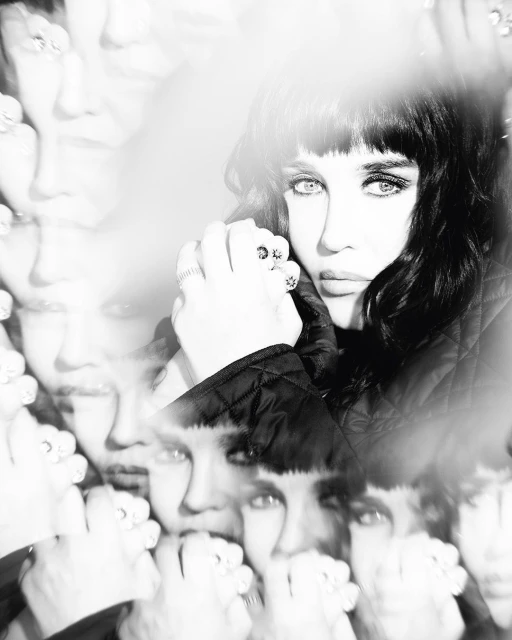 Black and white portrait of a woman with dark hair and bangs, wearing rings, with multiple superimposed face images and soft lighting.