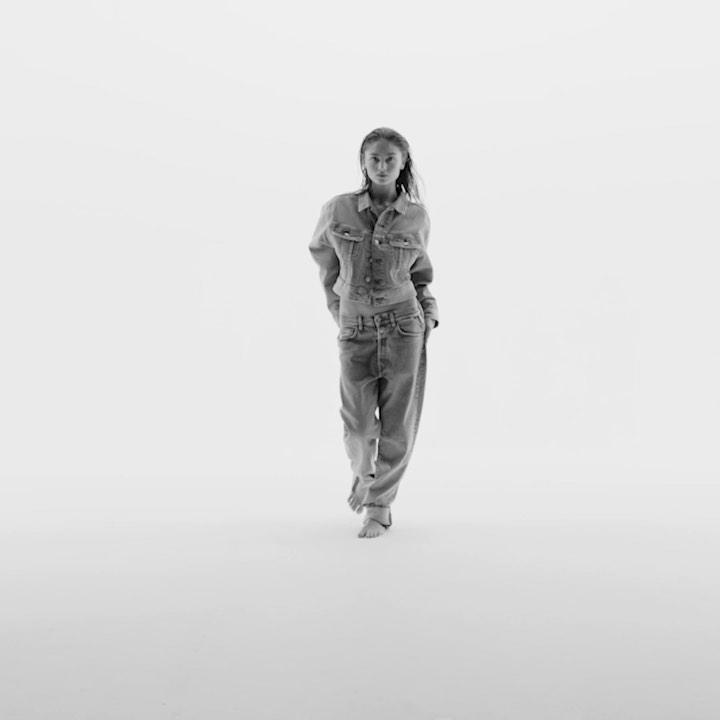 Model wearing denim jacket and jeans standing against a bright white background