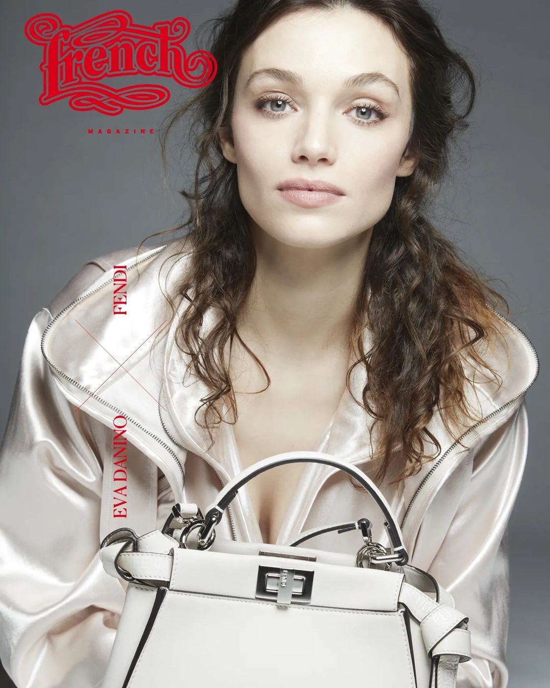 Magazine cover featuring a woman with curly hair wearing a light pink jacket and holding a white handbag against a grey background.