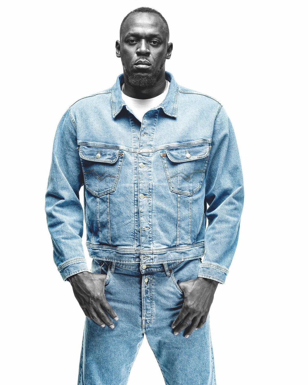 Portrait of Usain Bolt wearing a light blue denim jacket and matching jeans against a solid white background.