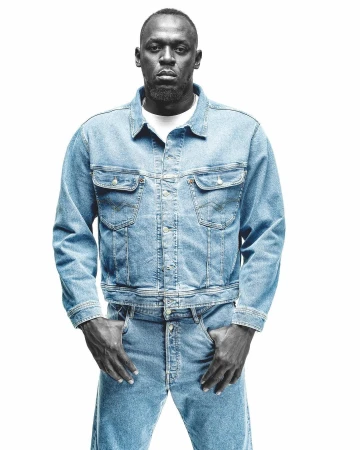 Portrait of Usain Bolt wearing a light blue denim jacket and matching jeans against a solid white background.