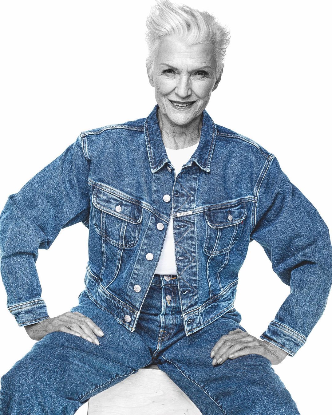 Elderly woman with white hair wearing a denim jacket and jeans against a white background