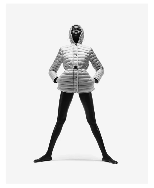 Fashion shot of an African woman wearing a white puffer jacket with a hood, standing in a wide stance against a bright white backdrop.