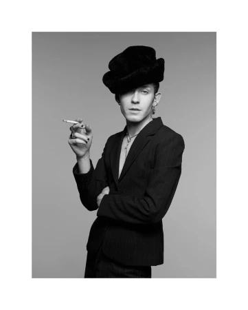 Man wearing a dark blazer, hat, and holding a cigarette against a grey seamless background