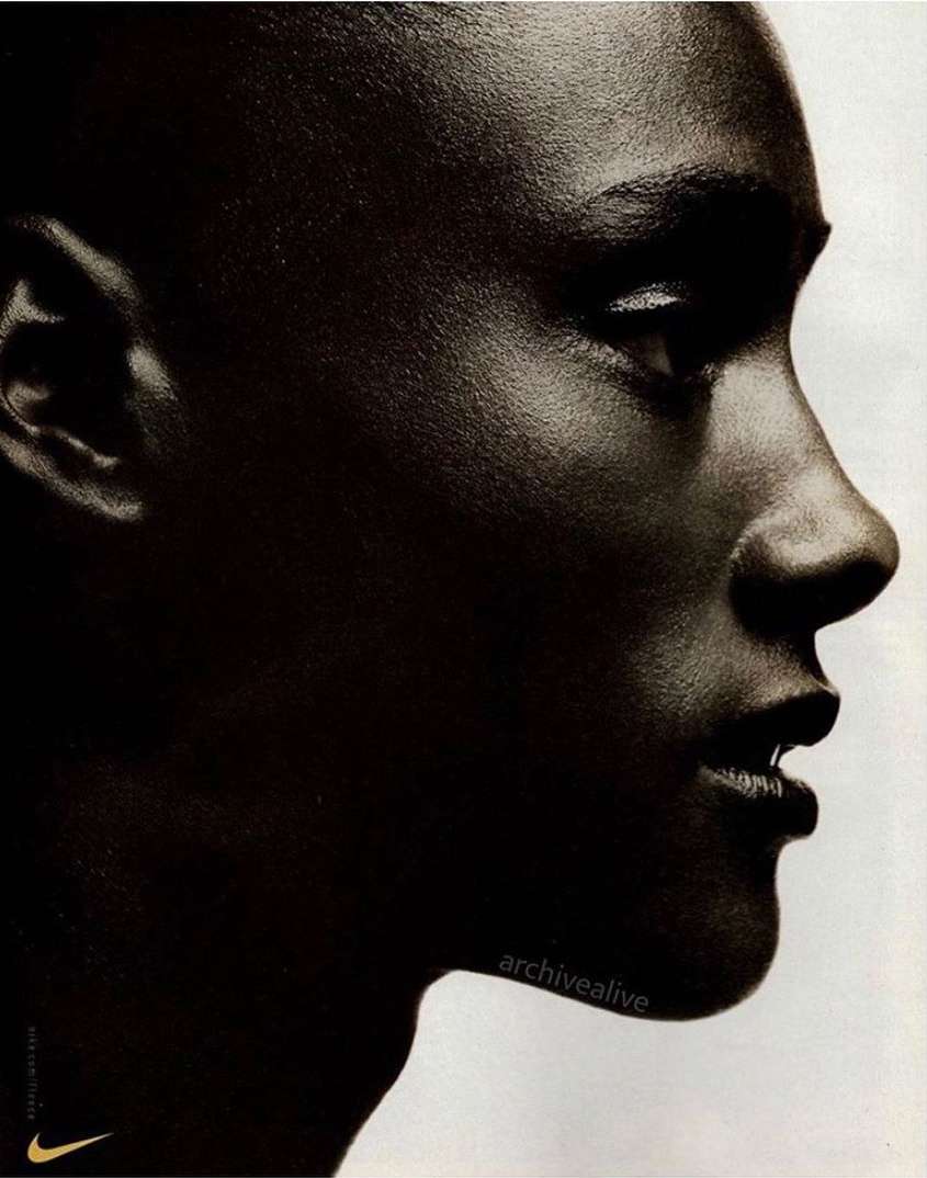 Close-up portrait of a Black adult woman with dark skin and dark hair, shown in profile against a light gray background.