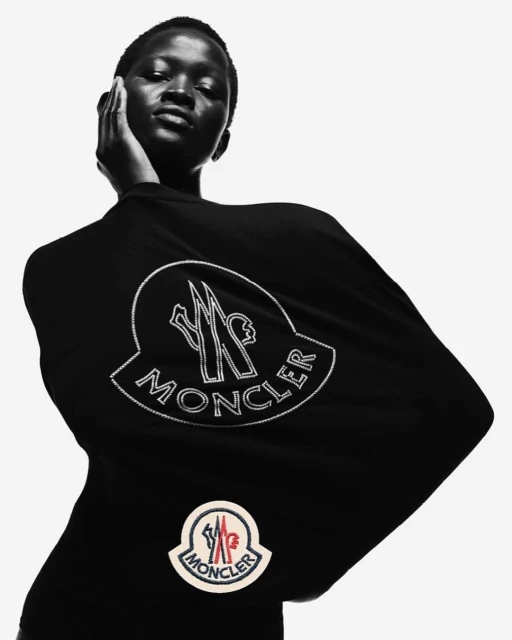 A woman poses in a black top with the Moncler logo against a white backdrop, showcasing fashion and brand visibility in monochrome.
