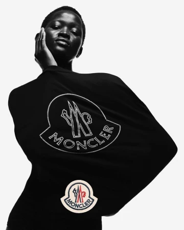 A woman poses in a black top with the Moncler logo against a white backdrop, showcasing fashion and brand visibility in monochrome.
