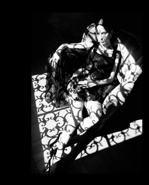 Black and white portrait of a woman reclining in an armchair, with dramatic lighting and shadow patterns from a decorative screen.