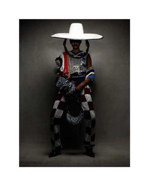 Fashionable person in checkered pants, knit top, and large hat in a studio shot, showcasing unique textures and design elements.