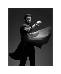 Monochrome portrait of a man in a structured coat swirling around him against a plain grey background