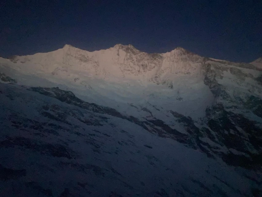 Snow-capped mountain range under a dark blue sky, illuminated by a soft glow, showcasing a serene natural landscape.