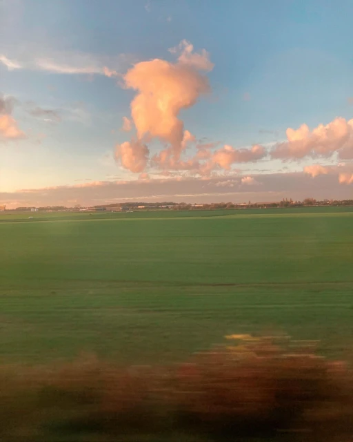 Green field landscape with a vibrant blue and orange sky filled with clouds at sunset, creating a picturesque nature scene.