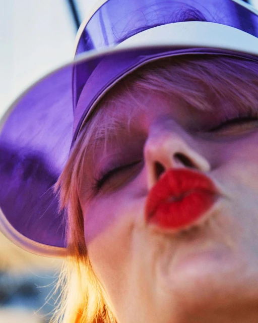 Blonde woman with purple visor and red lipstick puckers her lips in a close-up shot against a soft, blurred background.