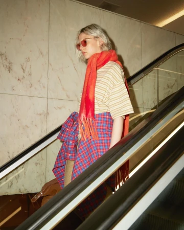 Model with tinted sunglasses and bright orange scarf descending an escalator in Paris by photographer Thierry Lebraly