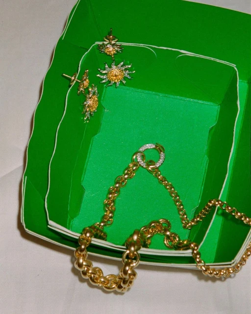 A green jewelry box with gold chains and jewelry with diamonds, shot with studio lighting on a white background, overhead shot.