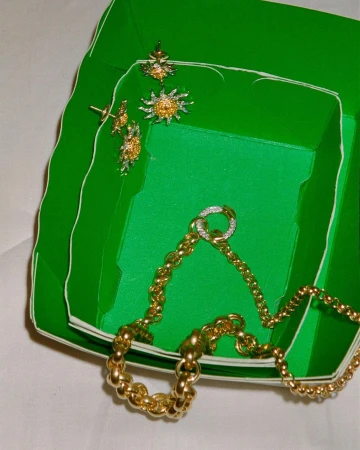 A green jewelry box with gold chains and jewelry with diamonds, shot with studio lighting on a white background, overhead shot.