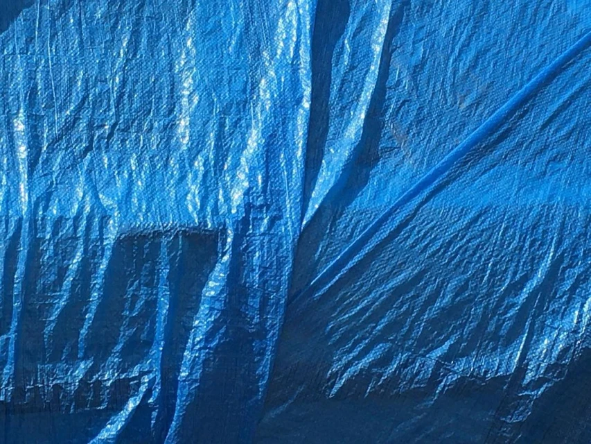 Close-up of a textured blue tarp with visible creases and folds, showcasing its durable, protective material and vibrant color.