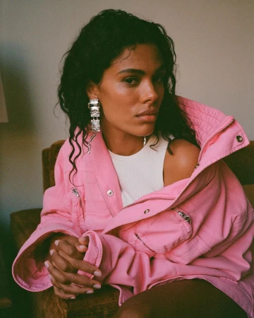 Woman wearing a pink jacket and large crystal earrings sitting indoors, photographed by Thierry Lebraly in Paris