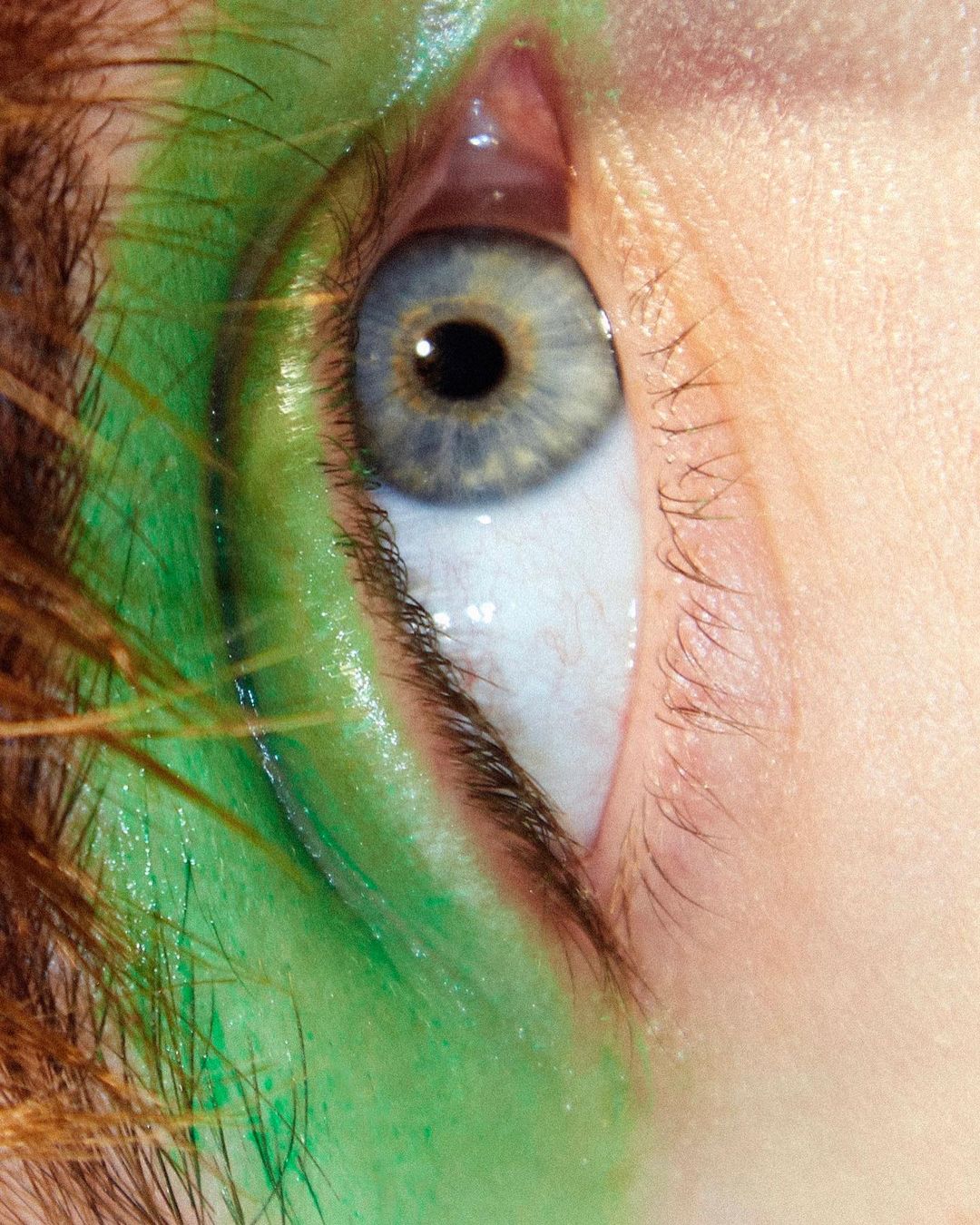 Extreme close-up of a woman's eye with creative bright green makeup on skin, featuring detailed lashes, brow, and skin textures.