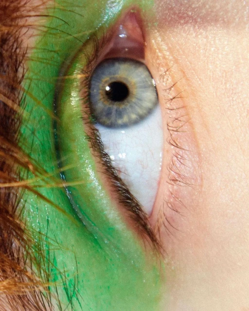 Extreme close-up of a woman's eye with creative bright green makeup on skin, featuring detailed lashes, brow, and skin textures.